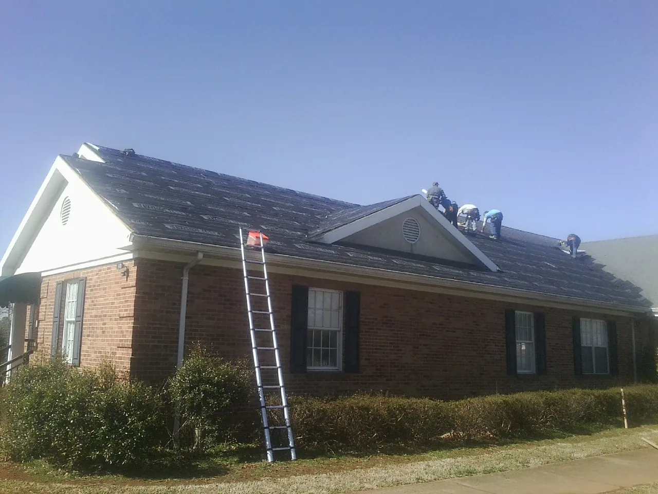 Crew tearing shingles off a brick ranch roof with a ladder set — Emergency Roof Repair work by our crew in Anoka