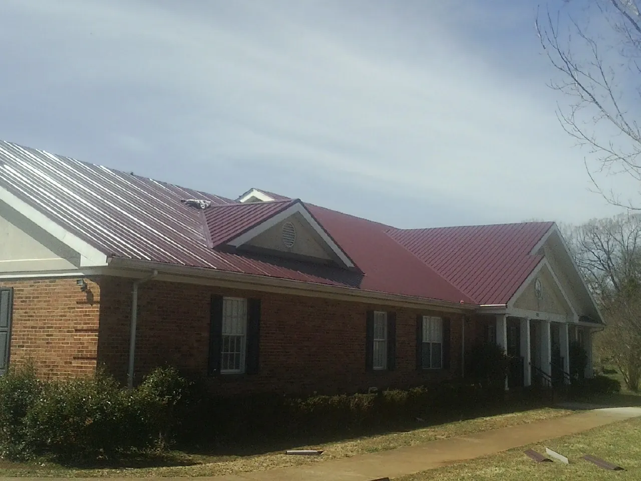 Red metal roof with gabled entries on a long brick building, from a Hail Damage Roof Repair job in Anoka
