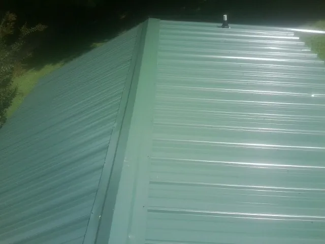 New green metal panels meeting at the ridge of a roof — Flat Roof Repair work by our crew in Anoka