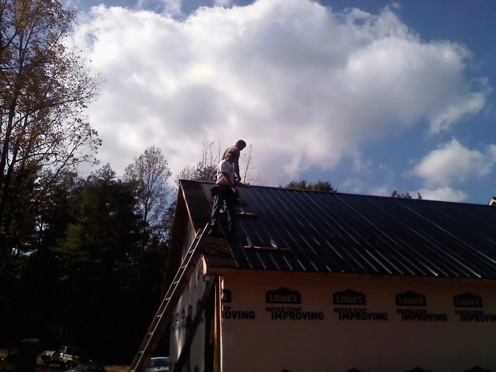 Roofer fastening dark metal panels high against a cloudy sky, from a Roof Inspection job in Anoka