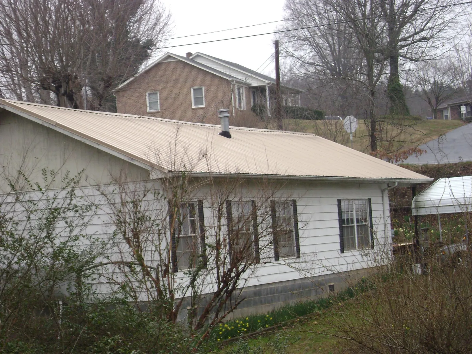 Tan metal roof on a white sided house set into a hillside — Commercial Roofing by Roofing Brothers in Anoka