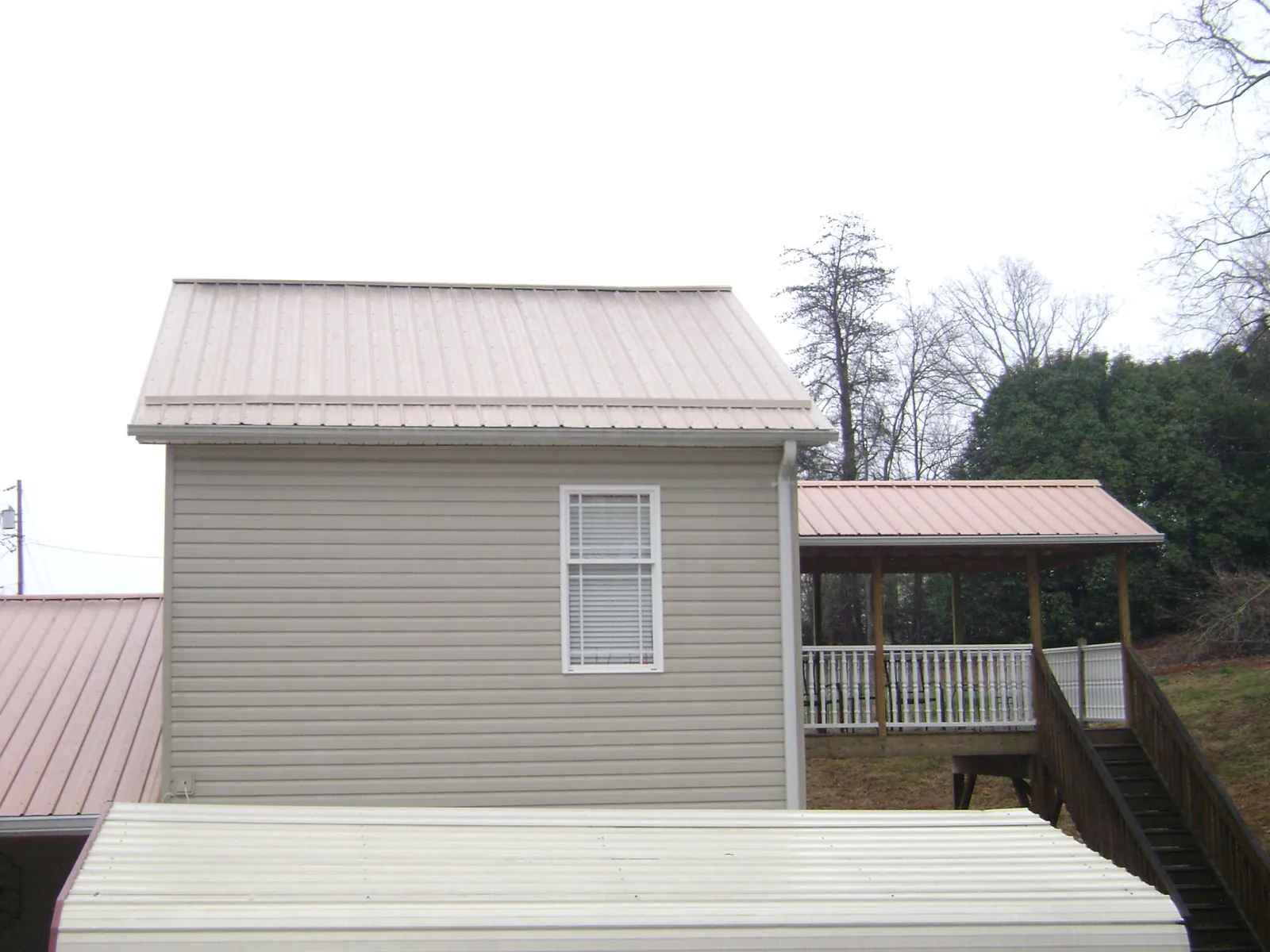 Tan metal roofs on a two story addition and attached porch, from a Roof Replacement job in Anoka